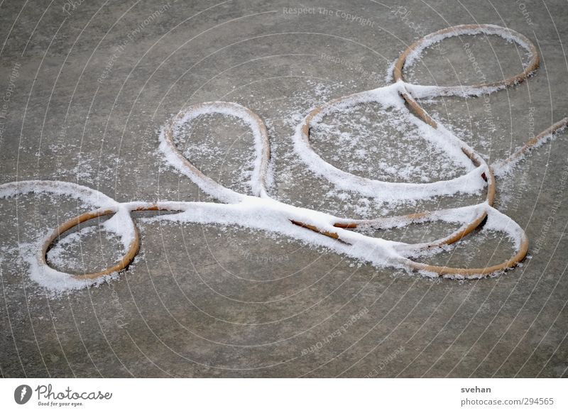 Schlängelndes Etwas Kabel Seil Beton Linie Schleife liegen grau weiß Schnee Schlaufe Winter Stromkabel durcheinander unordentlich Schlangenlinie Farbfoto