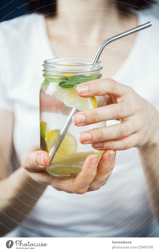 Frau hält ein Maurerglas mit frecher Zitrone und Minzwasser. Trinkhalm Metall Zitrusfrüchte Fokus selektiv Frühstück Getränk trinken Minze Limone Wasser