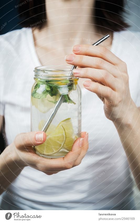 Frau hält ein Maurerglas mit frecher Zitrone und Minzwasser. Trinkhalm Metall Zitrusfrüchte Fokus selektiv Frühstück Getränk trinken Minze Limone Wasser Hand