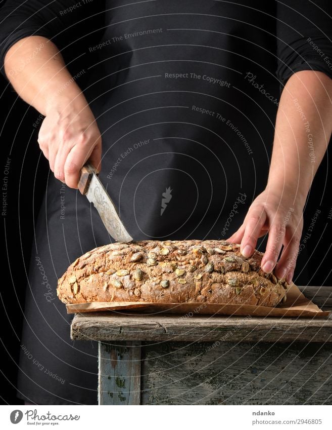 Frauenhände halten ovales, gebackenes Roggenbrot. Teigwaren Backwaren Brot Brötchen Ernährung Essen Frühstück Messer Tisch Küche Erwachsene Hand Wärme Holz