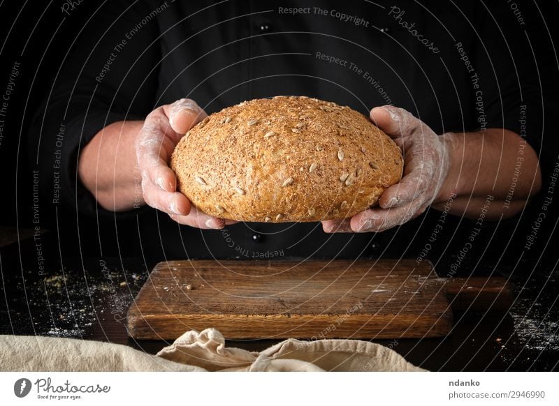 männliche Hände halten braun gebackenes Roggenbrot. Brot Ernährung Essen Mittagessen Abendessen Diät Tisch Küche Mann Erwachsene Hand Holz festhalten dunkel