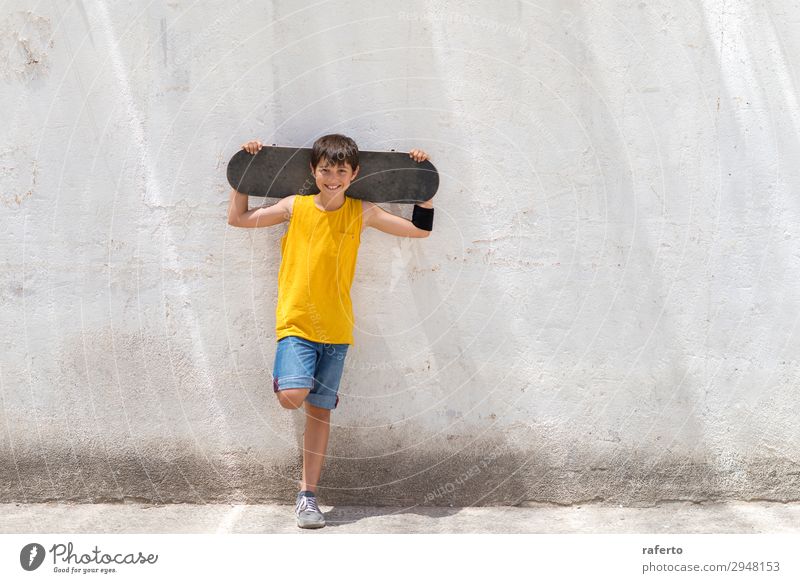 Junger lächelnder Junge, der sich an eine gelbe Wand lehnt und ein Skateboard hält. Stil Glück Kind Mensch maskulin Junger Mann Jugendliche 1 Schönes Wetter