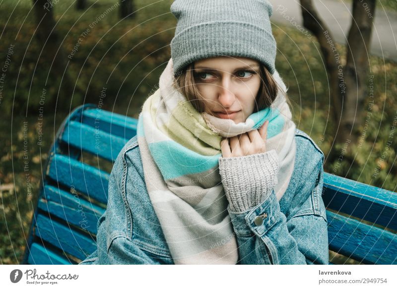 junge erwachsene Frau, die auf einer Bank sitzt, die mit einem Schal umwickelt ist. Erwachsene Einsamkeit attraktiv Herbst schön Kaukasier kalt Jeansstoff Wald