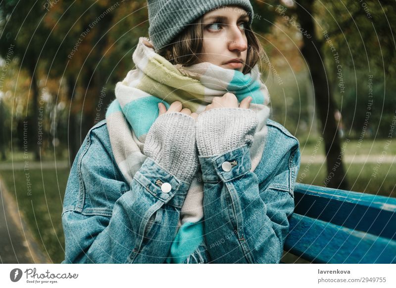 junge erwachsene Frau, die auf einer Bank sitzt, die mit einem Schal umwickelt ist. Einsamkeit Baum Hut Jeansstoff kalt Außenaufnahme Model Behaarung Erwachsene