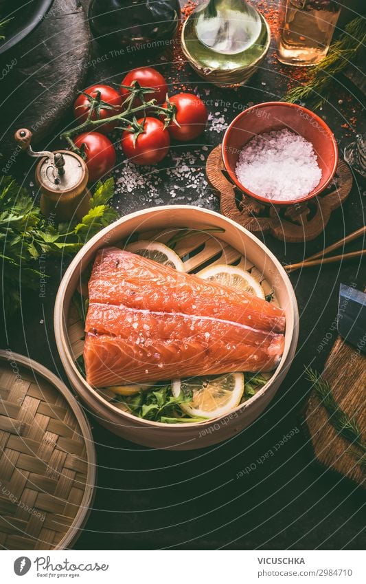 Rohes Lachsfilet im Bambusdämpfer auf dunklem, rustikalem Küchentisch mit frischen Zutaten und Werkzeugen. Gesundes Essen und Kochen. Diät-Konzept. Asiatische Küche. Zubereitung der Speisen