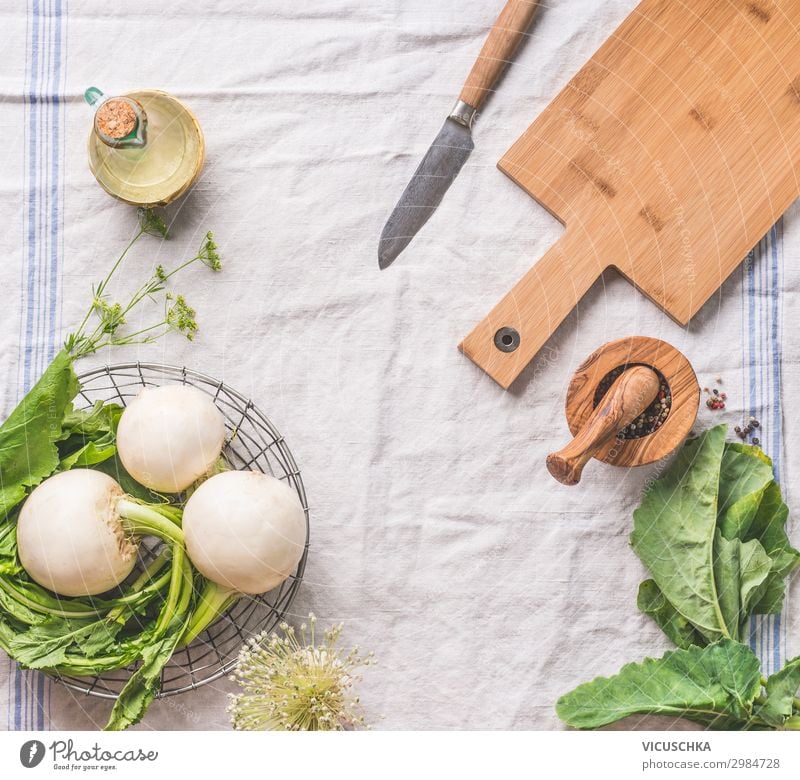 Lebensmittelhintergrund mit roher junger Rübe mit Grünzeug auf hellem Küchentisch mit Schneidebrett und Messer, Draufsicht. Gesundes vegetarisches Ess- und Kochkonzept. Kopierraum für Ihr Design