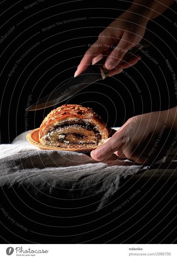 weibliche Hände schneiden gebackenes Brötchen mit Mohnblättern Teigwaren Backwaren Brot Dessert Messer Körper Tisch Frau Erwachsene Hand Holz Essen dunkel