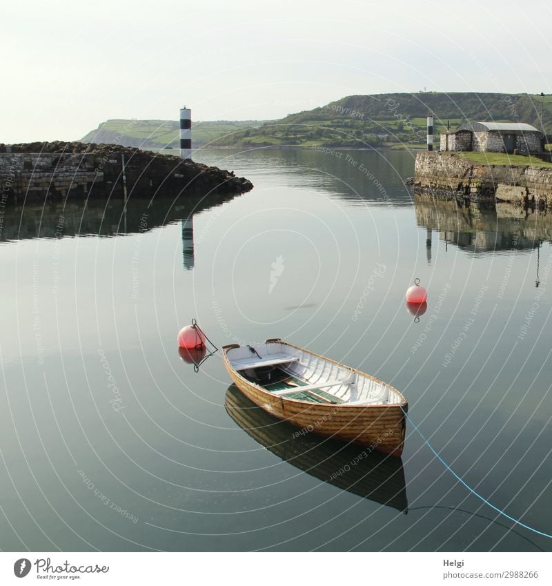 in einem kleinen Hafen in Irland liegt ein Holzboot in stillem Wasser mit Spiegelung, im Hintergrund ein schwarz-weißer Leuchtturm Umwelt Natur Landschaft