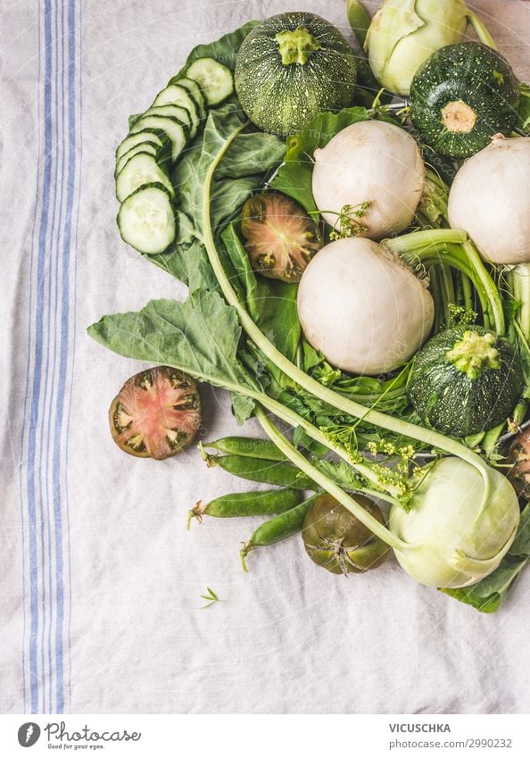 Verschiedene grüne Gemüsehaufen auf hellem Tisch : grüne Erbsen, Kohlrabi, Salat, Zucchini, Gurke, grüne Tomaten. Ansicht von oben. Sauberes vegetarisches Ess- und Kochkonzept. Lokales Gemüse vom Bauernhof