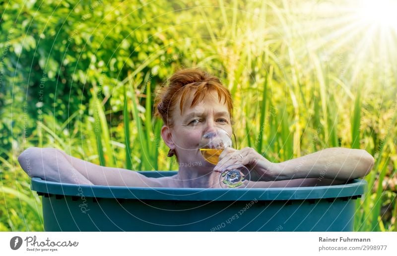 Bei hohen Temperaturen und Sonnenschein im Sommer badet eine Frau in einer Regentonne. In der Hand hält sie ein Glas mit Weißwein. Mensch feminin Erwachsene