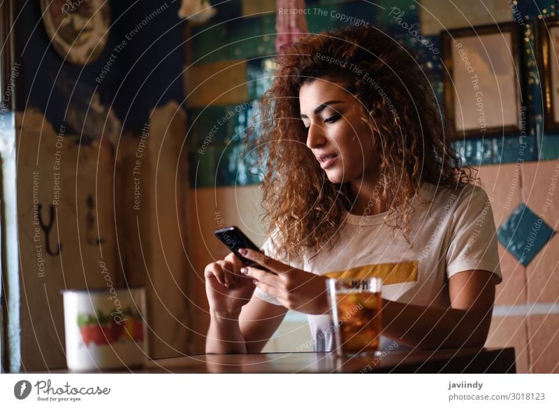 Junge arabische Frau mit schwarzer Lockenfrisur sitzt in einer schönen Bar mit Vintage-Dekoration Getränk trinken Lifestyle Stil Haare & Frisuren