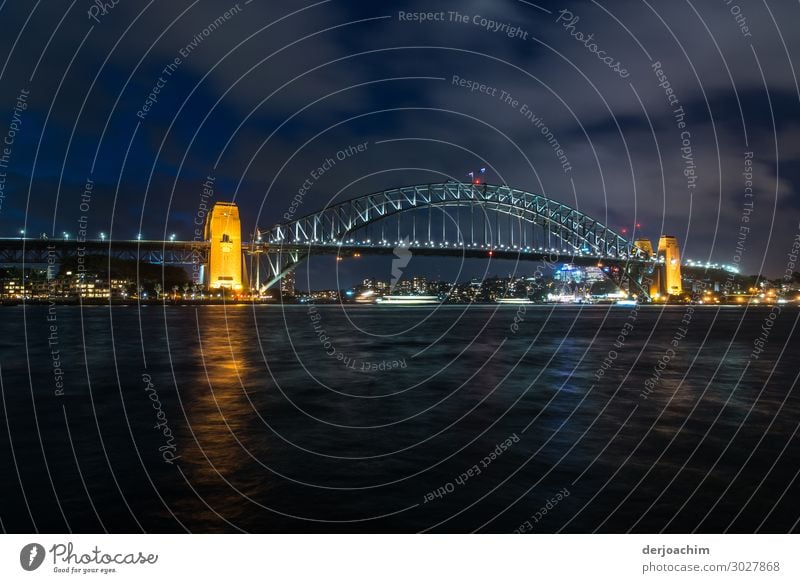 Sydney -Brücke bei Nacht . Im Vordergrund das Meer. Hinten im Bild die erleuchtete Brücke mir gelb angeleuchteten Pfeilern. Ausflug Sommer Wasser Schönes Wetter