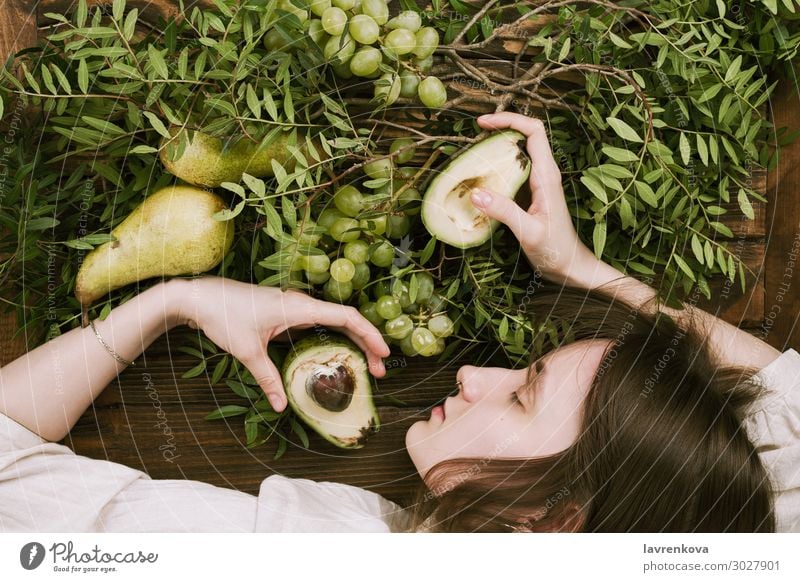 Frau, die auf einem Holztisch liegt und Trauben, Birnen und Avocados hält. Landwirtschaft Ackerbau Ast Bauernhof flache Verlegung Lebensmittel Gesunde Ernährung