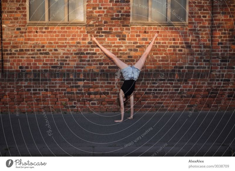 Frau macht einen Radschlag vor einer Backsteinmauer auf dem Gehweg Lifestyle elegant Stil Freude schön Leben Wohlgefühl Spielen Radschlagen Junge Frau