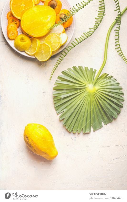 Ganze Papayafrucht auf weißem Tisch mit tropischen Blättern und Teller mit gelben, geschnittenen Früchten, Draufsicht. Sommerliches Essen. Gesunde Ernährung. Teller mit Frühstücksfrüchten. Platz zum Kopieren. Modern. Flach liegend