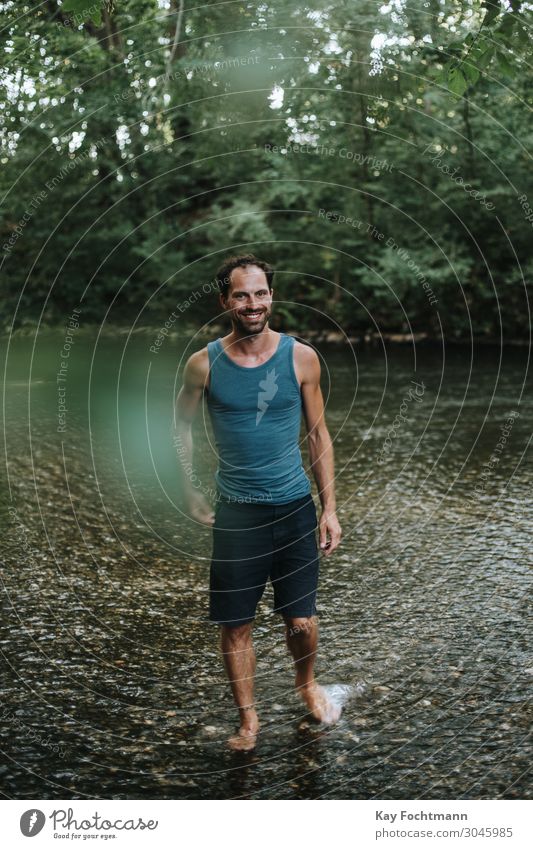 glücklicher Mann, der durch das Wasser eines Flusses watet 30s Erwachsener Vollbart sorgenfrei lässig Kaukasier heiter Selbstvertrauen selbstbewusst cool