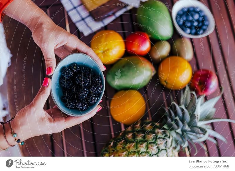 eine junge Frau, die eine Schüssel Brombeeren hält. Sie bereitet ein gesundes Rezept aus verschiedenen Früchten, Wassermelone, Orange und Brombeeren zu. Verwendung eines Mixers. Hausgemacht, drinnen, gesunde Lebensweise