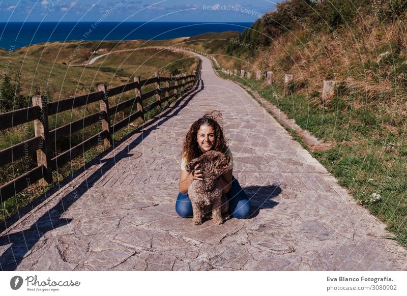 junge Frau und ihr süßer spanischer Wasserhund im Freien, die gemeinsam an einem sonnigen und windigen Tag genießen. Sommerzeit, Tierliebe und Ferienkonzept