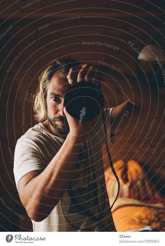 Der Fotograf Lifestyle Wohnung Spiegelreflexkamera Objektiv Junger Mann Jugendliche 30-45 Jahre Erwachsene T-Shirt blond langhaarig Bart festhalten Coolness