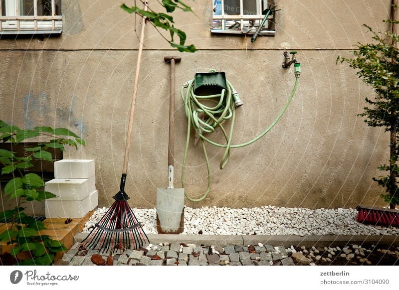 Garten im Hinterhof Gartengeräte Schlauch Gartenschlauch Wasser Wasserhahn Wasserschlauch Spaten Schaufel Häusliches Leben Wohnhaus Fassade Fenster Gitter Kies