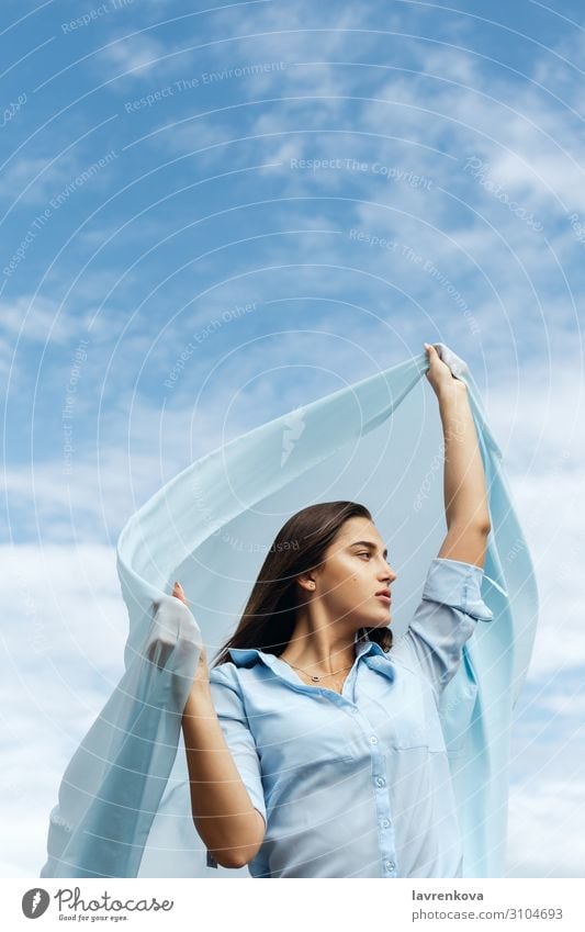 Junge Frau, die einen Schnitt aus blauem Stoff am Himmel hält. Erwachsene Luft Einsamkeit attraktiv Wolken geschnitten Freiheit Hand Glück Höhe Horizont Natur