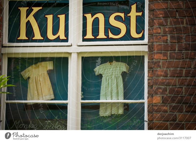 Das Wort Kunst steht hinter einem  Fenster mit Rahmen. Hinter dem Fenster zwei kleine Kleider. Stil Ausflug Dekoration & Verzierung Sommer Schönes Wetter Stadt