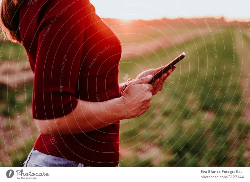 Nahaufnahme einer schönen kaukasischen Frau, die den Sonnenuntergang auf dem Land beobachtet. Mit dem Mobiltelefon. Technologie und Lebensstil im Freien