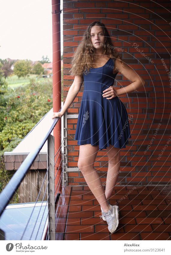 Portrait einer jungen, großen Frau auf einem Balkon mit Ziegelsteinmauer und Aussicht auf den Garten Lifestyle Stil schön Leben Wohnung Haus Backstein