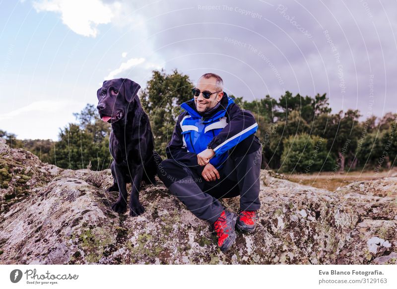 junger Wanderer am Berg mit seinem schwarzen Labrador auf dem Gipfel eines Felsens. bewölkter Wintertag Natur Unbekümmertheit gehorsam Jugendliche Glück Zunge