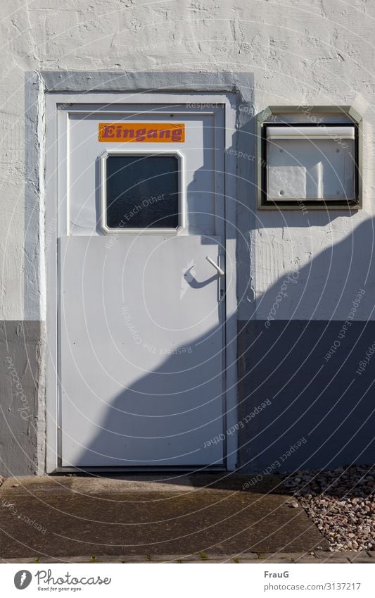 Eingang Gebäude Wand Putz Fassade Tür Eingangstür geschlossen Fenster Griff schräg Türgriff Türschloss Schild Schrift Schaukasten leer Schatten Kies