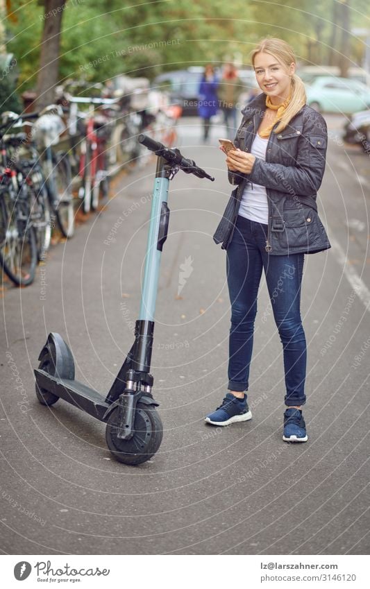 Junge blonde Frau, die in der Nähe des elektrischen Tretroller steht. Lifestyle Glück schön Freizeit & Hobby Technik & Technologie Erwachsene 1 Mensch Verkehr