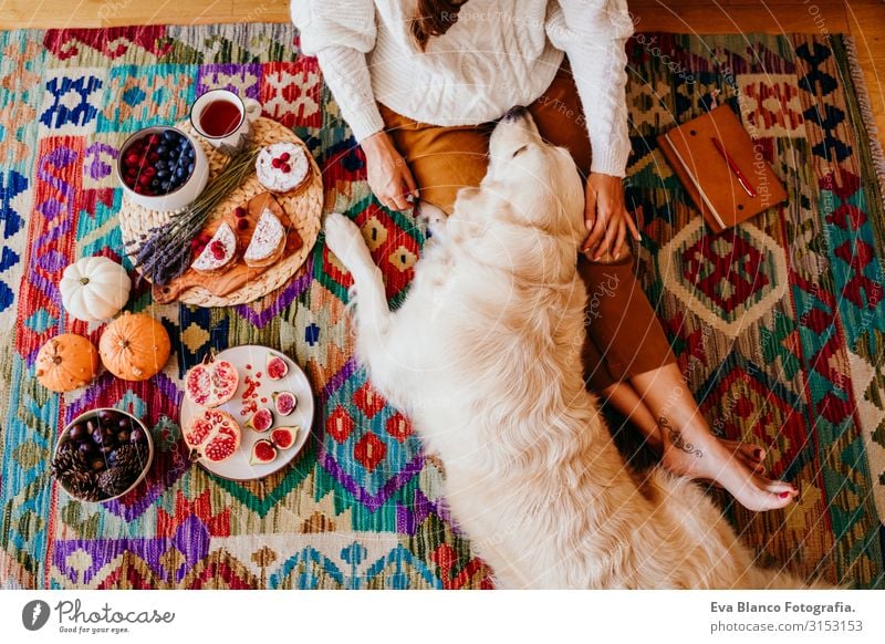 schöne Frau, die während des gesunden Frühstücks zu Hause eine Tasse Kaffee genießt. Schreiben auf einem Notizbuch. Außerdem ist der Golden Retriever-Hund bezaubernd. Lebensstil im Haus