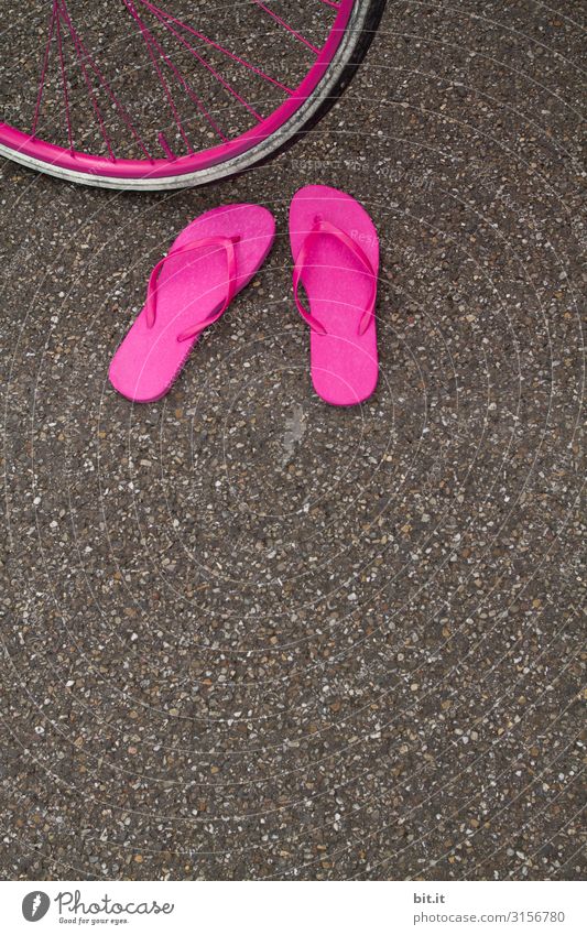 Ein Paar fnallige pinke Flip Flops, stehen herrenlos im Sommer auf dem Asphalt der Straße, vor einem Fahrradreifen in Pink und warten auf ihren Besitzer.