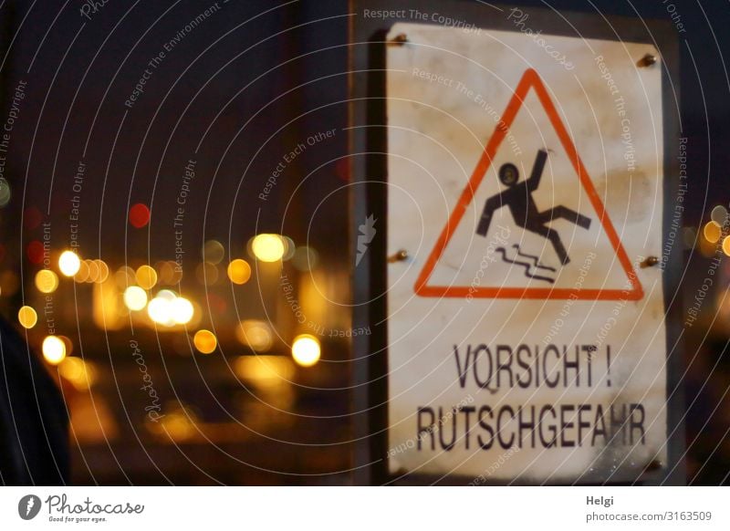 Warnschild "Vorsicht Rutschgefahr" mit leuchtendem Bokeh vor dunklem Hintergrund Stadt Kunststoff Zeichen Schriftzeichen Hinweisschild festhalten Kommunizieren