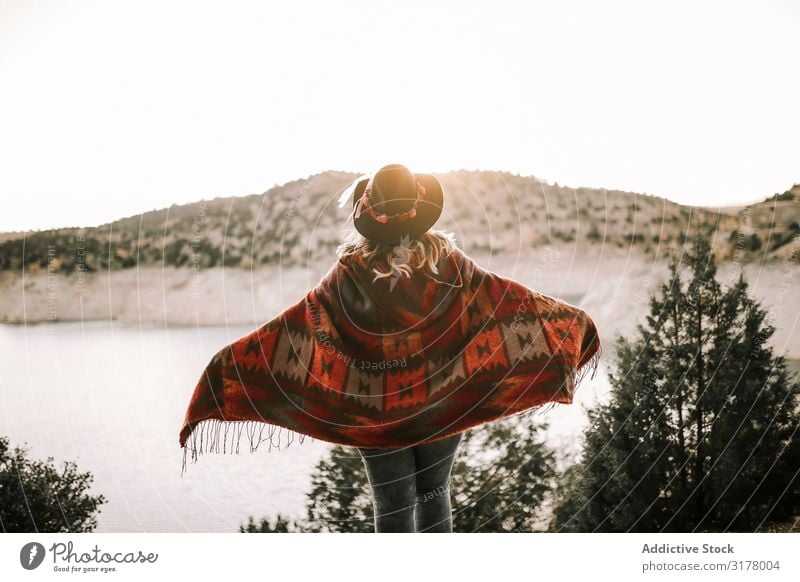 Anonyme Frau am ruhigen See bei Sonnenaufgang Himmel Berge u. Gebirge Ferien & Urlaub & Reisen bewundernd Morgen Freiheit Landschaft Poncho Hut Unbekümmertheit