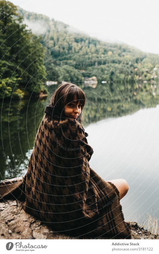 Frau sitzt mit Decke in der Nähe von See und Bergen. sitzen Berge u. Gebirge malerisch Wasser Küste Oberfläche erstaunlich Aussicht Hügel Stein Himmel Wolken