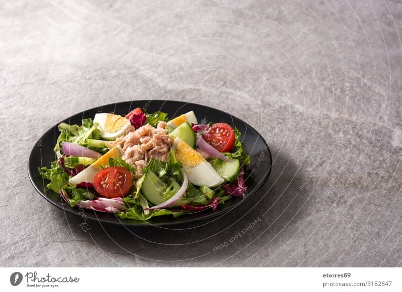 Salat mit Thunfisch, Ei und Gemüse auf schwarzem Teller Salatbeilage Tomate Kopfsalat Zwiebel Gurke Salatgurke Scheibe gemischt Olivenöl Gesunde Ernährung