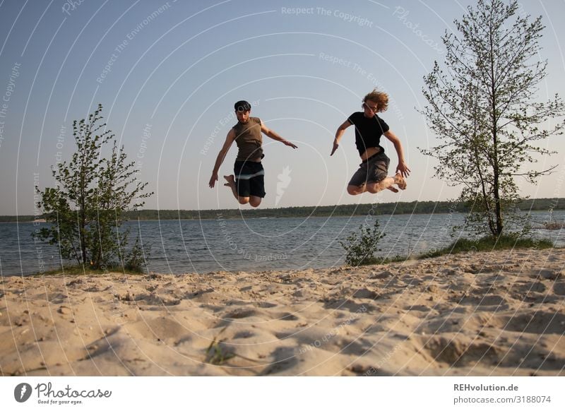 2 Männer springen an einem See in die Luft Tag Bewegung Erwachsene 18-30 Jahre Jugendliche Mensch Freude Außenaufnahme Farbfoto Ganzkörperaufnahme