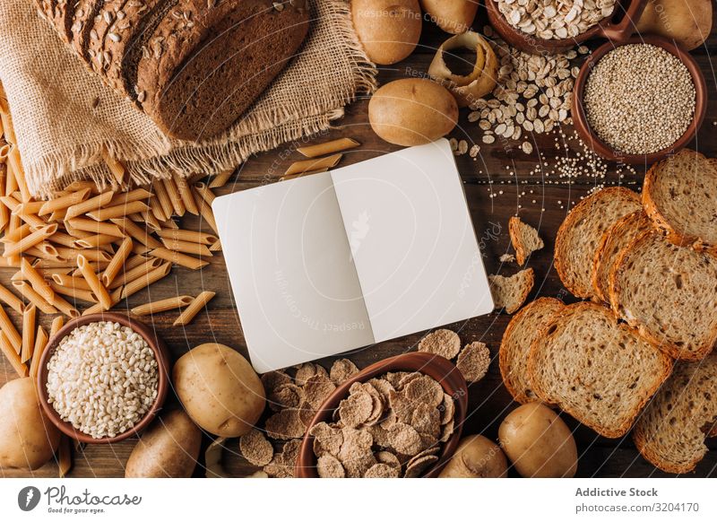 Vollkornprodukte und frisch gebackenes Roggenbrot auf dem Tisch Brot Kartoffeln Haferflocken Zerealien Mahlzeit Haferbrei Notizbuch appetitlich geschmackvoll