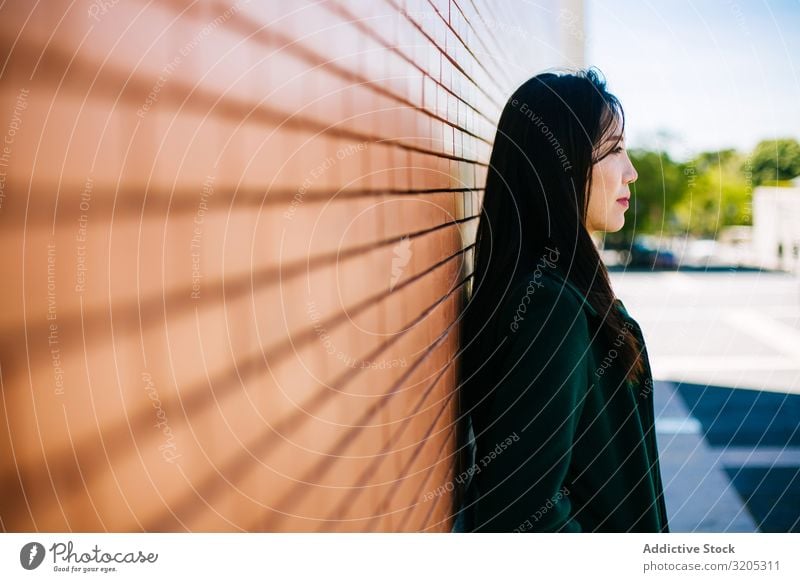 Nachdenkliche Asiatin, die an einer Ziegelmauer lehnt Frau Wand anlehnen besinnlich Wegsehen Straße Großstadt asiatisch urwüchsig Relief Oberfläche Lifestyle