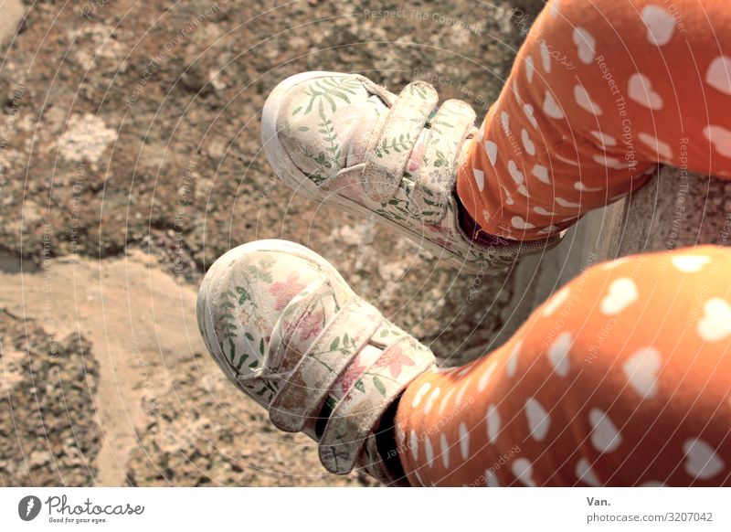 Walking in my shoes Kind Mädchen Beine Fuß 1 Mensch Mauer Wand Hose Schuhe sitzen orange Herz geblümt Muster Stein Boden Farbfoto Gedeckte Farben Außenaufnahme