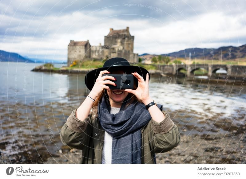 Lächelnde, reisende Frau beim Fotografieren mit dem Telefon Schottland fotografierend Smartphone Natur gealtert Burg oder Schloss Kosten See trendy benutzend