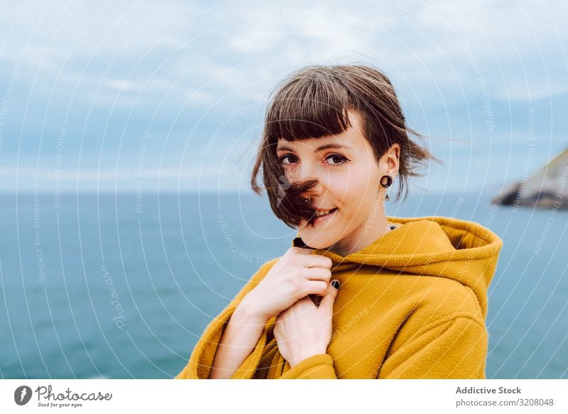 Junge Frau steht am Meer MEER wolkig Himmel reisen Jacke warm Natur Freizeit Lifestyle Ufer Küste Wasser blau jung Ausflug Reise Tourismus Dame froh zufrieden