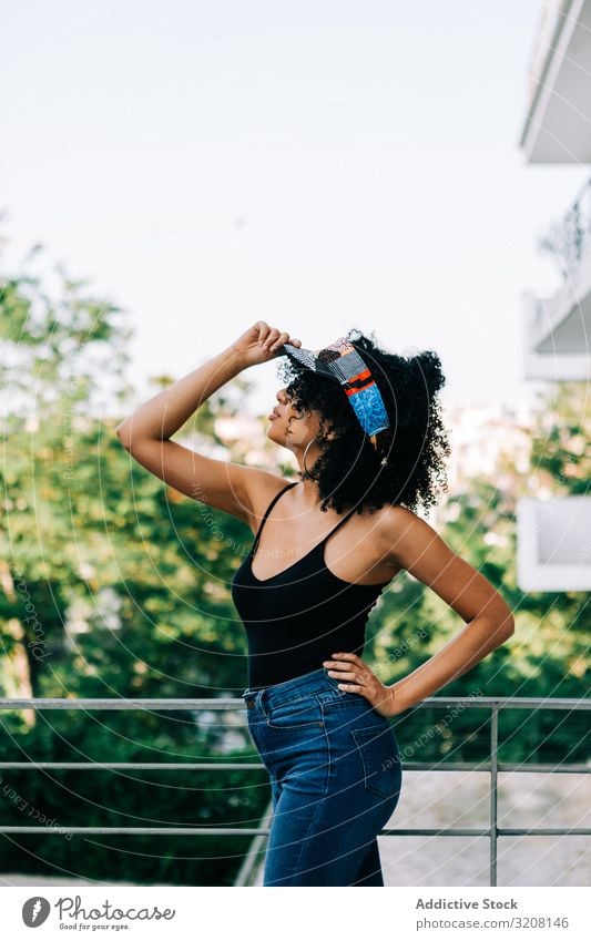 Hübsche ethnische Frau am Metallgeländer modisch stylisch trendy glamourös Bekleidung Outfit Stirnband Jeanshose Tanktop jung Afroamerikaner lässig schön hübsch