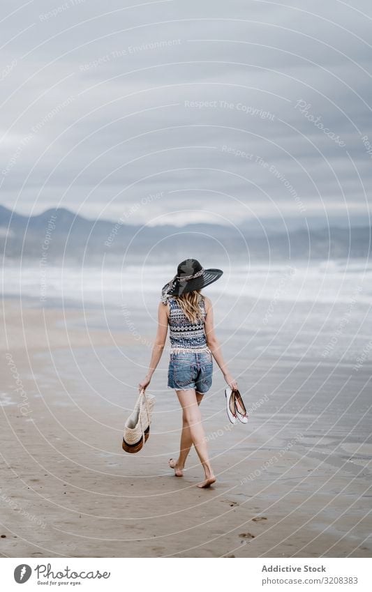 Junge Frau geht barfuss am Sandstrand Hut Strand Tasche modisch glamourös Meer Sommer Urlaub reisen Erholung Feiertag Landschaft malerisch jung Person attraktiv