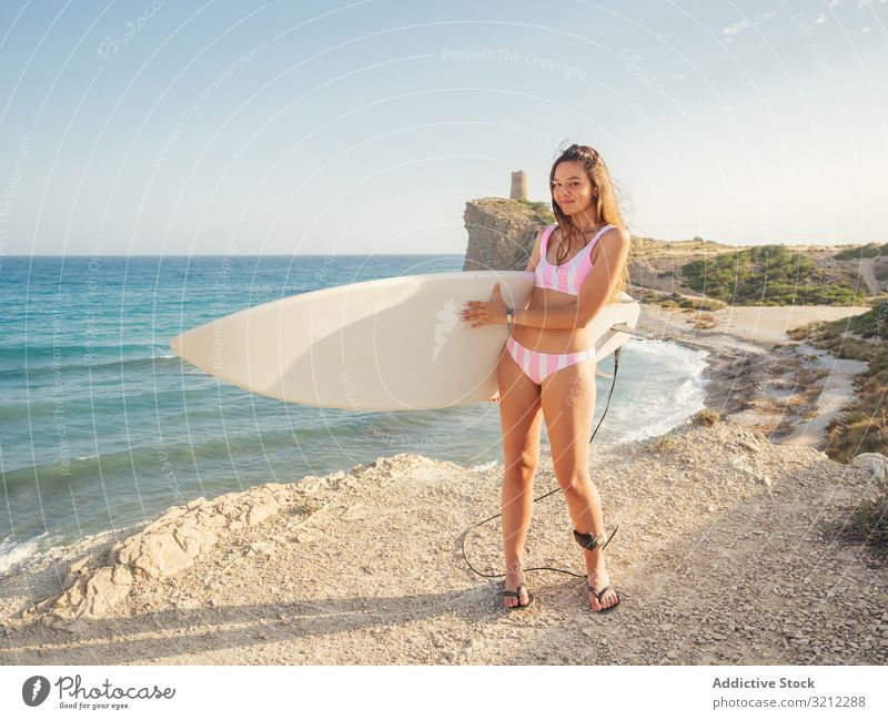 Frau hebt Surfbrett hoch und bleibt an der Meeresküste Strand Badeanzug PKW Bräune Seeküste Urlaub schlank Sonnenbad aktiv Sport Lifestyle MEER Sommer attraktiv