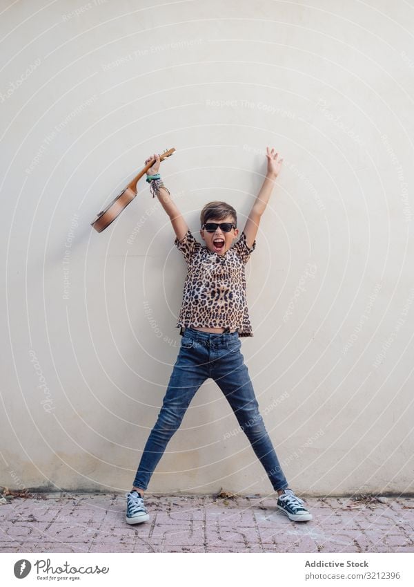 Aufgeregtes Kind hebt die Hände mit der Ukulele Spaß haben Junge Spielen dekorativ Instrument farbenfroh Musical niedlich Entertainment üben schön Sonnenbrille