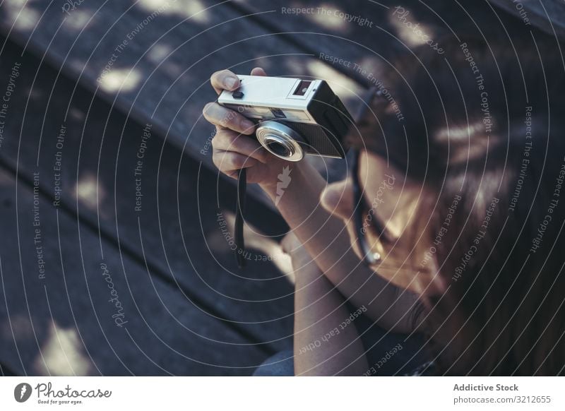 Frau mit Fotokamera sitzt und schaut an einem sonnigen Tag mit Natur Bank professionell lässig Freizeit Lifestyle Fotografieren Feiertag Sommer Hobby digital