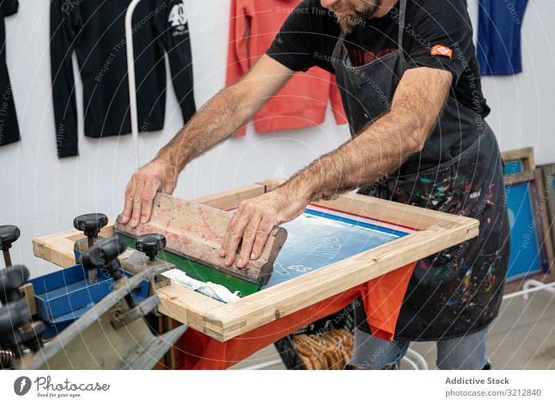 Männlicher Künstler erstellt Druck auf T-Shirt Meister Bildschirm drucken Siebdruck Serigraphie erschaffend Werkstatt Hobby Staffelei dreckig Schürze Stil Farbe