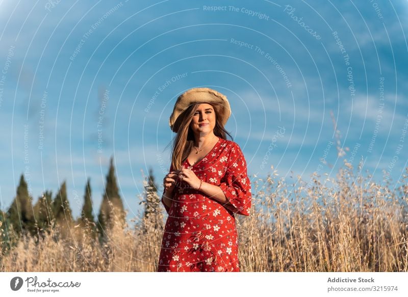 Glückliche verträumte Frau steht im hohen Gras Feld attraktiv Lächeln Strohhut rotes Kleid blau Himmel Natur Sommer jung Lifestyle positiv Fröhlichkeit charmant